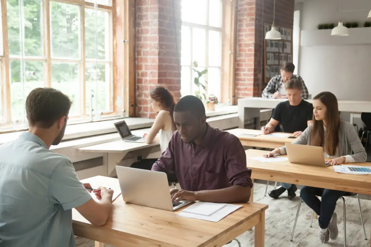 Coworkers using laptops at shared tables in an open office