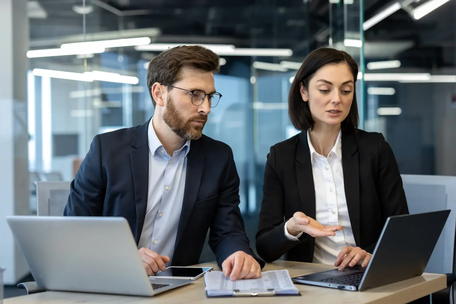Two finance professionals reviewing reports on laptops